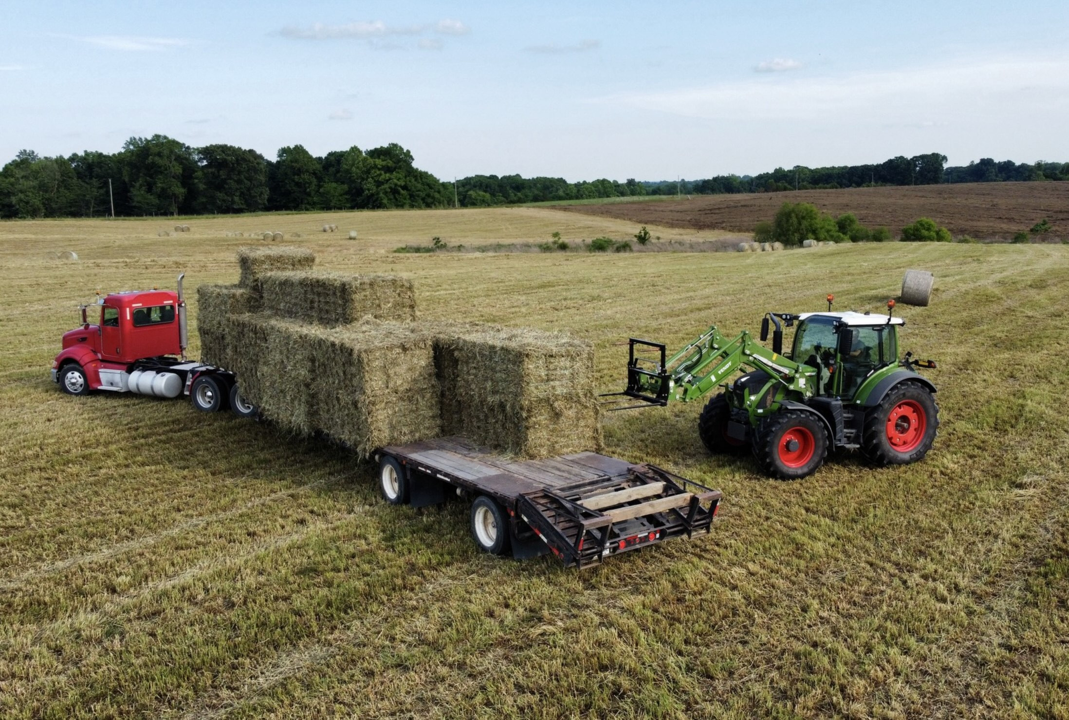Large farm equipment in a big field loading newly harvested bales of hay.