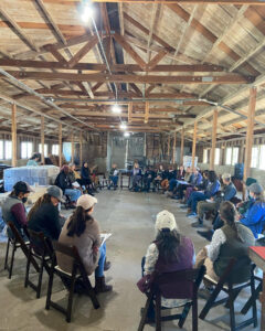 Women in agriculture sit in circle in barn.