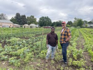 A Boise refugee farmer and white male stand in farm field.