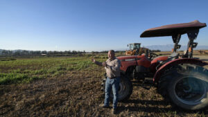 A farmer talks in front of a red tractor which is parked in a newly planted field. 