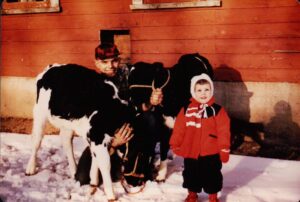 Chelsea Gazillo and her grandfather in a red barn with a black and white cow.